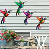 Four iridescent metal hummingbird wall decor birds in vibrant colors perched on a wooden surface.