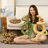 A woman is holding a large, realistic green snake plush toy with yellow accents in a living room setting.