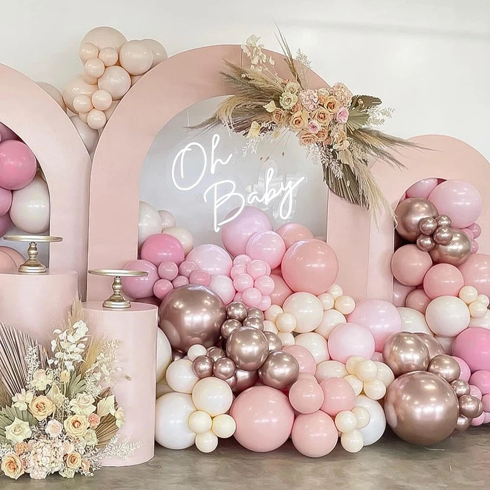 A display of pastel pink and beige latex balloons arranged in an arched backdrop for a baby shower or party.