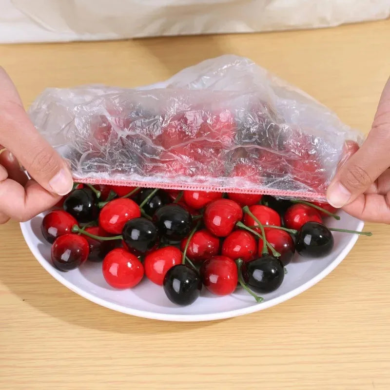 Hands are holding a clear plastic wrap covering a plate of mixed red and black berries.