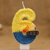 A birthday candle shaped like the number 6, decorated with yellow glitter and a construction excavator face on a blue base.