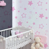 A white crib decorated with pink star vinyl wall decals and a teddy bear toy.