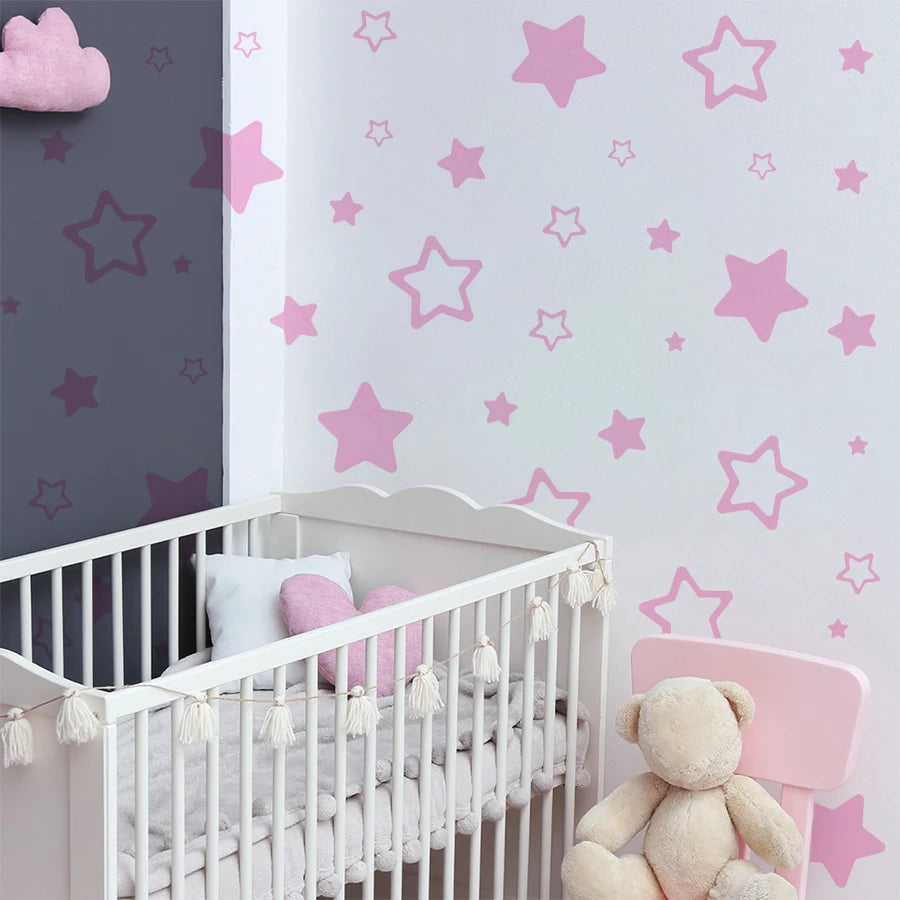 A white crib decorated with pink star vinyl wall decals and a teddy bear toy.