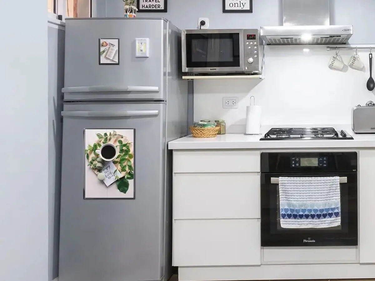 A silver refrigerator and a white kitchen counter display magnetic picture frames on the wall.