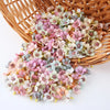 A pile of silk artificial flower heads in soft pink, peach, and pale blue colors resting in a woven basket.