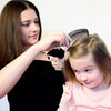 A woman is using an anti-dandruff scalp massage comb on a young girl's hair.