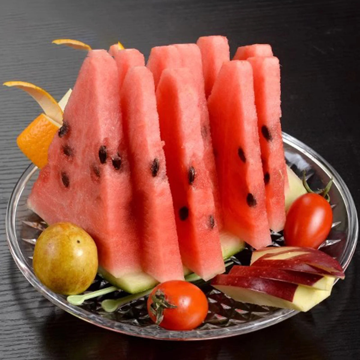 Sliced watermelon served on a clear acrylic plate with garnishes.