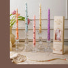 A collection of tall, decorative printed candles in pink and purple hues displayed on a light surface.