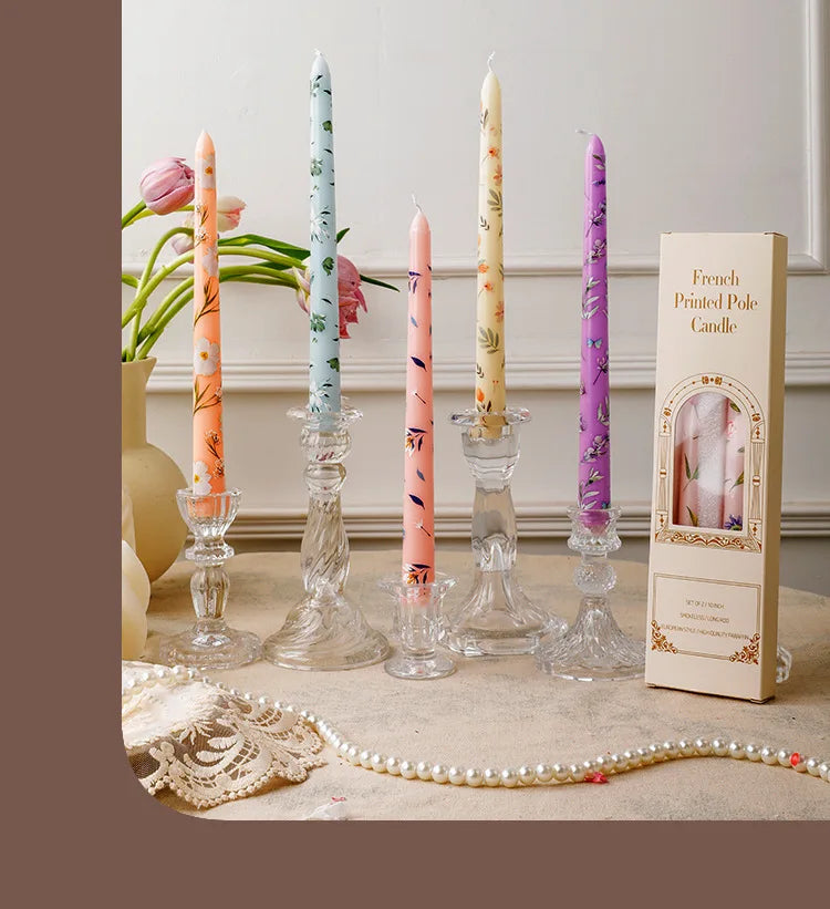 A collection of tall, decorative printed candles in pink and purple hues displayed on a light surface.