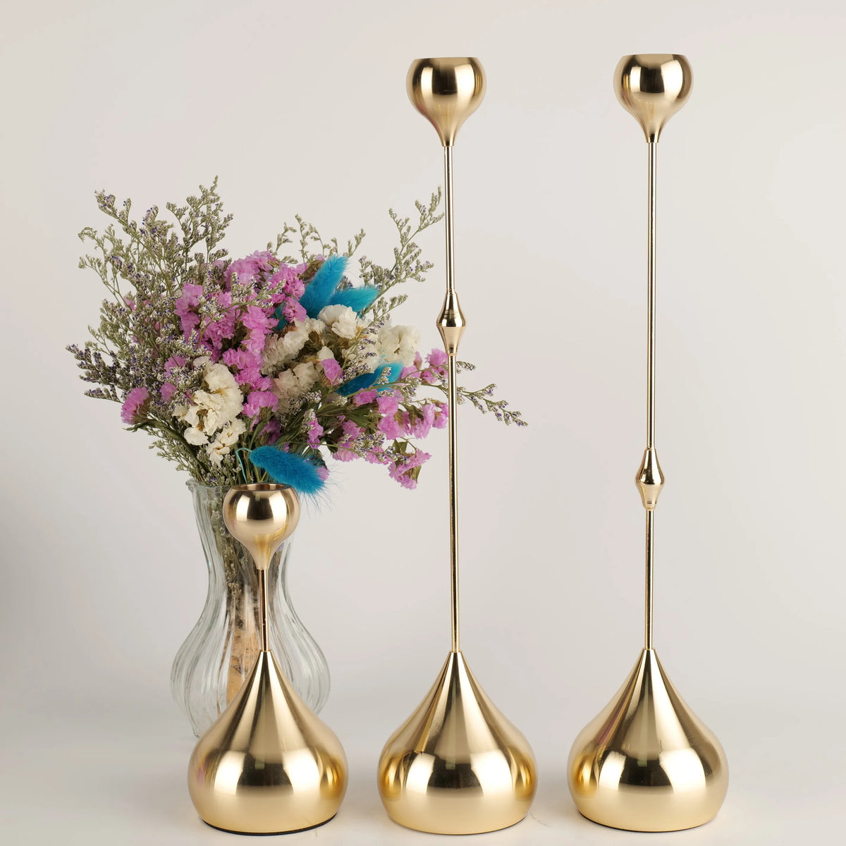 A set of three gold waterdrop design candle holders with slender stems and flared bases displayed against a light background.