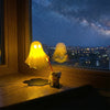 A glowing yellow ghost figurine and a small dog figurine sit on a wooden desk next to a window with a night sky view.