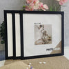 A set of three black photo frames with white mats displayed on a beige surface.