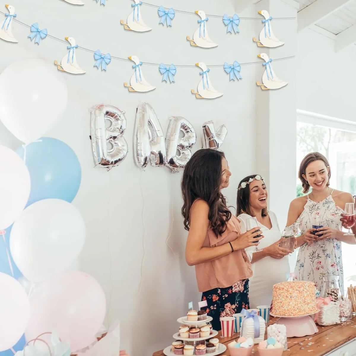 A woman in a pink top is holding a glass while another woman smiles next to a banner decorated with white and blue bowknot ga