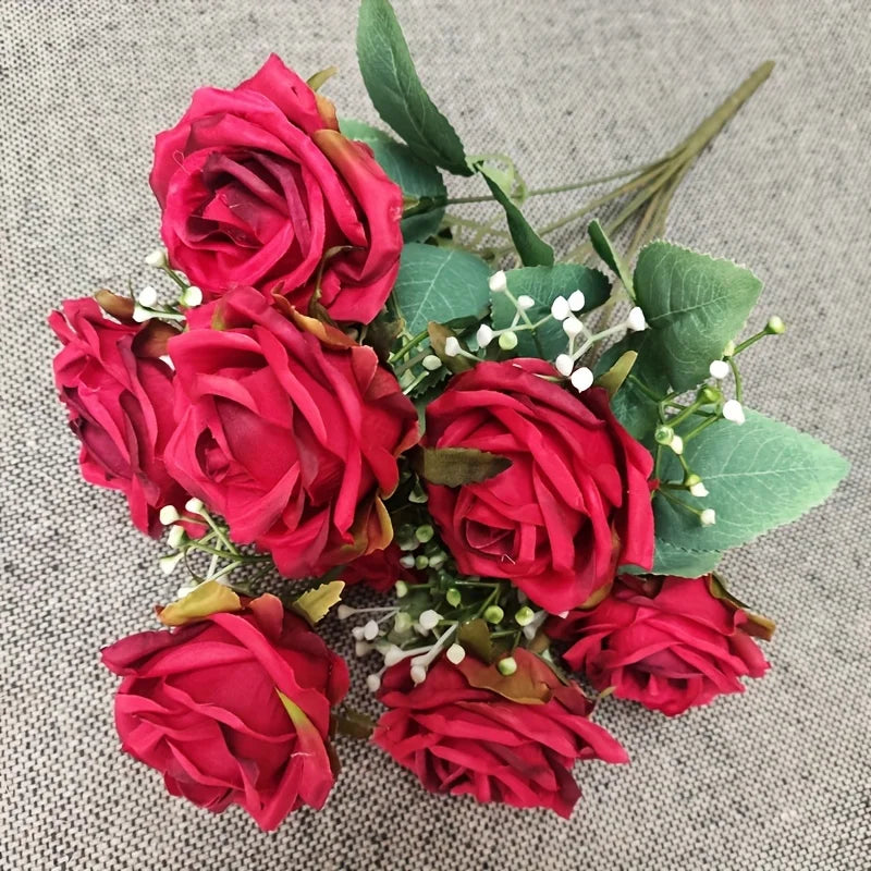 A bouquet of deep red silk roses with green foliage and small white filler flowers.