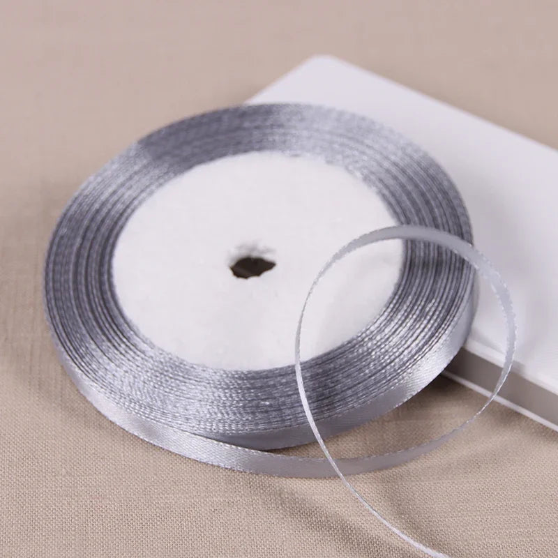 Silver satin ribbon spool with a thin ribbon unwound on a white background