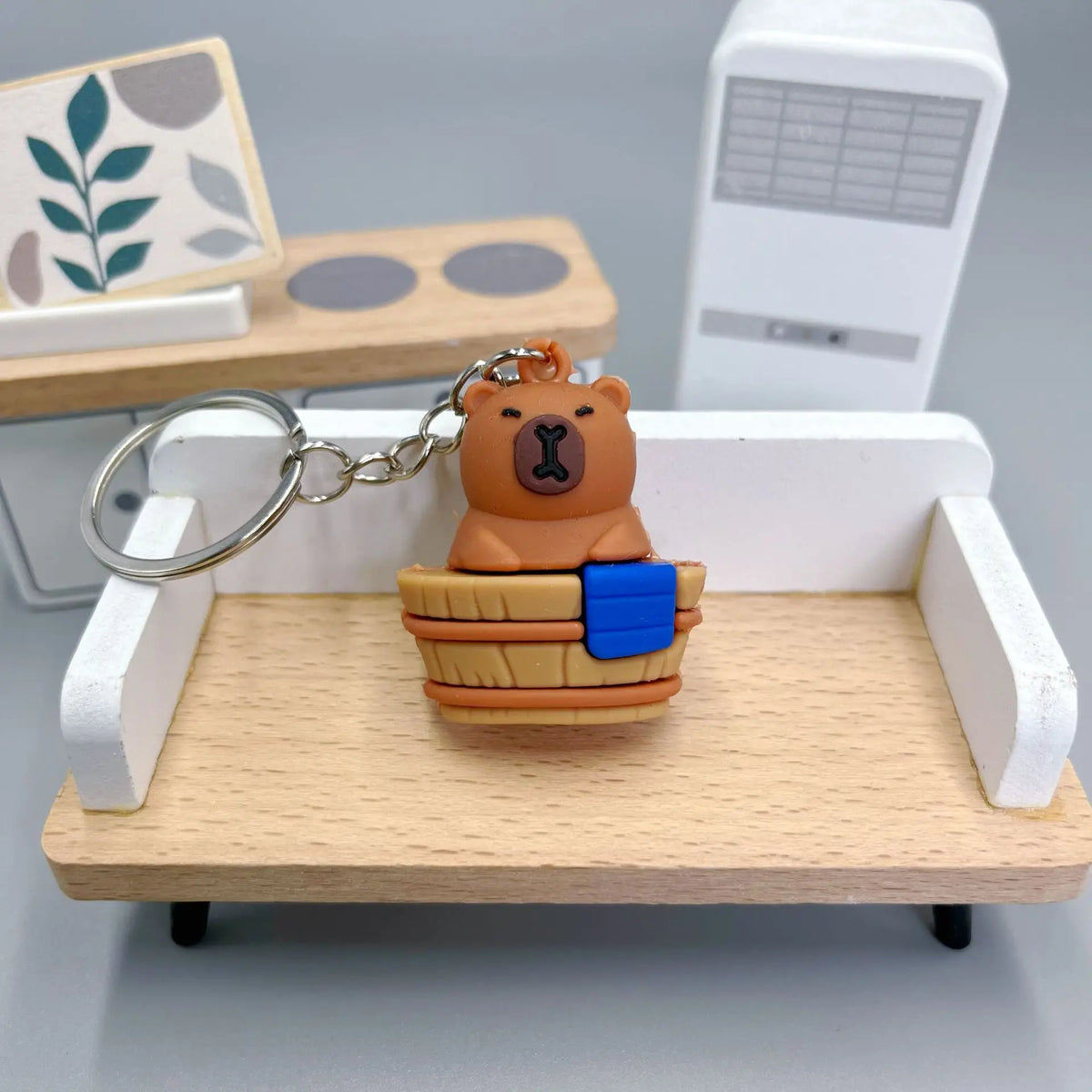 Un pendentif de clé en forme de capybara orange est exposé sur une étagère en bois à côté d'une boîte rectangulaire blanche.