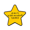 A yellow star enamel pin with black outline featuring the text didn't bite anyone today