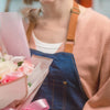 A person is holding a pink flower arrangement wrapped in decorative paper.