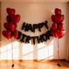 A decorative banner made of black heart balloons spelling out HAPPY BIRTHDAY hanging on a white wall.