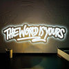 A glowing neon sign on a textured wall reads The World Is Yours.