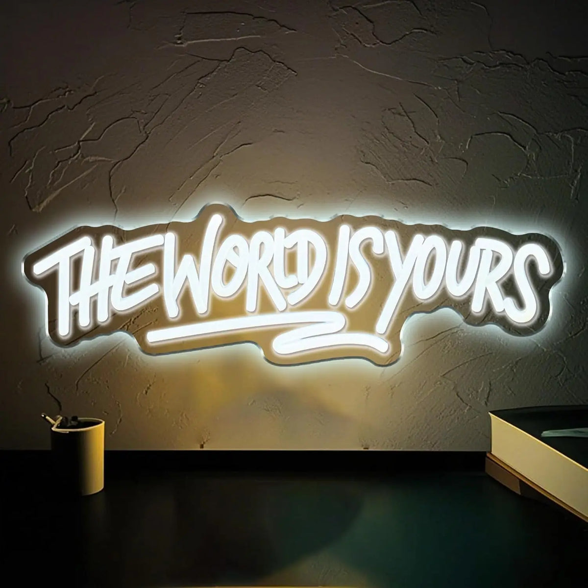 A glowing neon sign on a textured wall reads The World Is Yours.