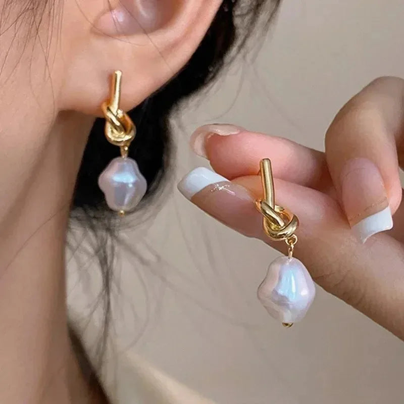 Elegant gold bean spliced pearl drop earrings worn by a hand against dark hair.