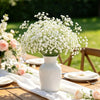 A white ceramic vase filled with artificial baby's breath flowers on a wooden table.