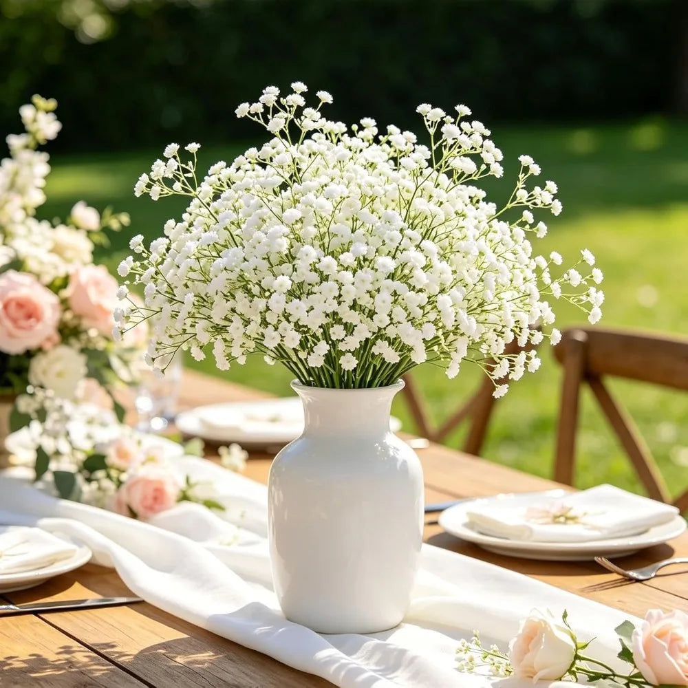 A white ceramic vase filled with artificial baby's breath flowers on a wooden table.