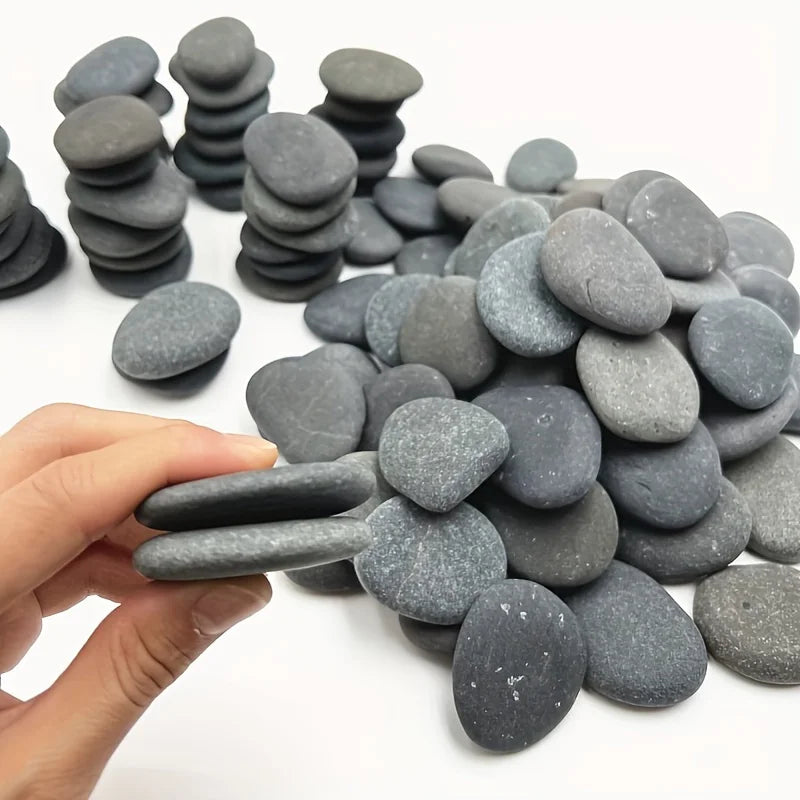 A hand holds a pile of smooth, gray river rocks used for aquariums or art projects.