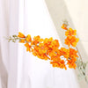 Une branche de fleurs artificielles de delphinium orange vif avec du feuillage vert sur fond blanc.