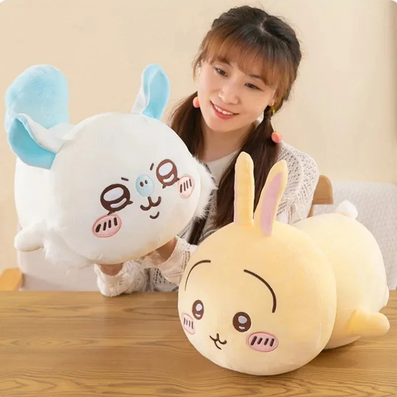 A woman is holding a white and blue Chiikawa Hachiware plush pillow, a soft anime cuddle toy, on a wooden table.