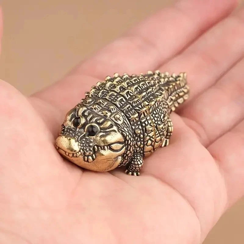 A small, textured copper alligator desk decor is held in a person's hand.