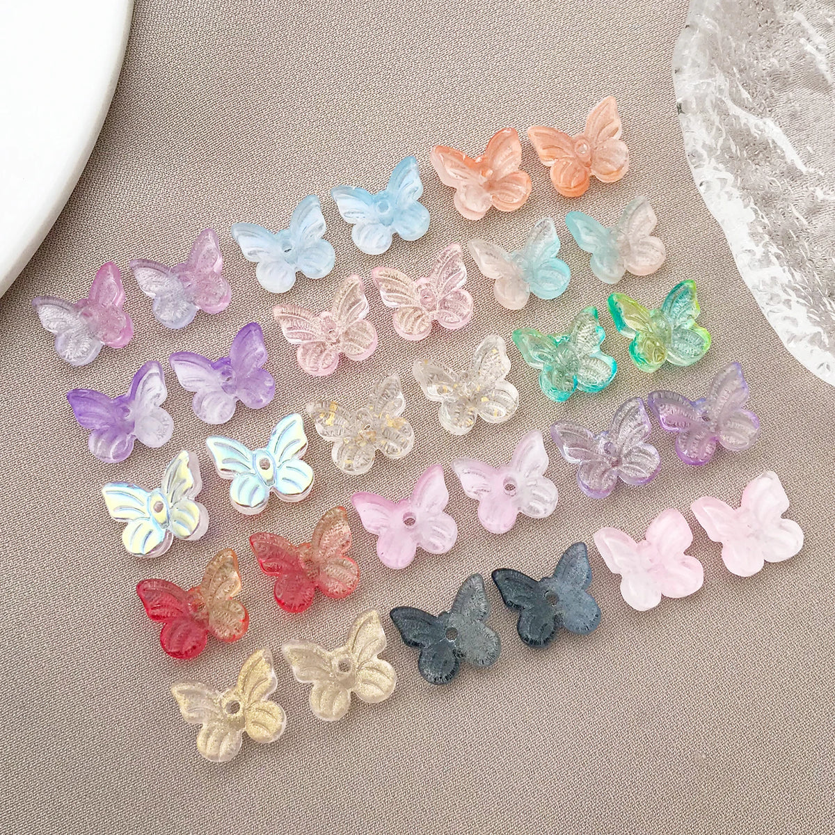 Variedad de cuentas de mariposa de vidrio coloridas dispuestas en línea diagonal sobre fondo neutro.