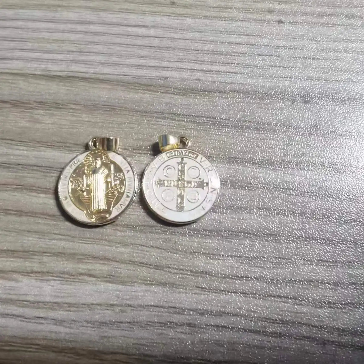 A pair of silver religious pendants featuring St. Benedict imagery, used for crafting or gifting.