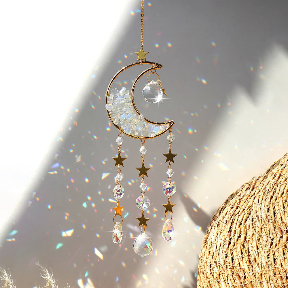 A gold crescent moon dreamcatcher hangs, featuring clear crystals and rainbow prisms, against a bright sunlit background.