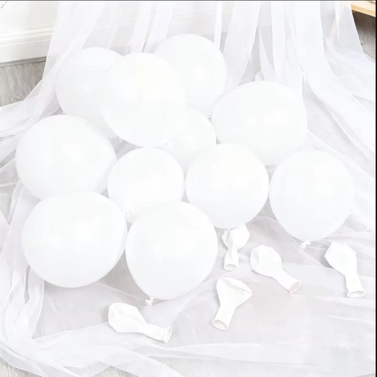 A collection of white latex balloons arranged on sheer white fabric for celebrations
