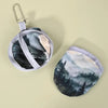 A round handheld cooling fan with a light gray fabric and a dark forest landscape design.