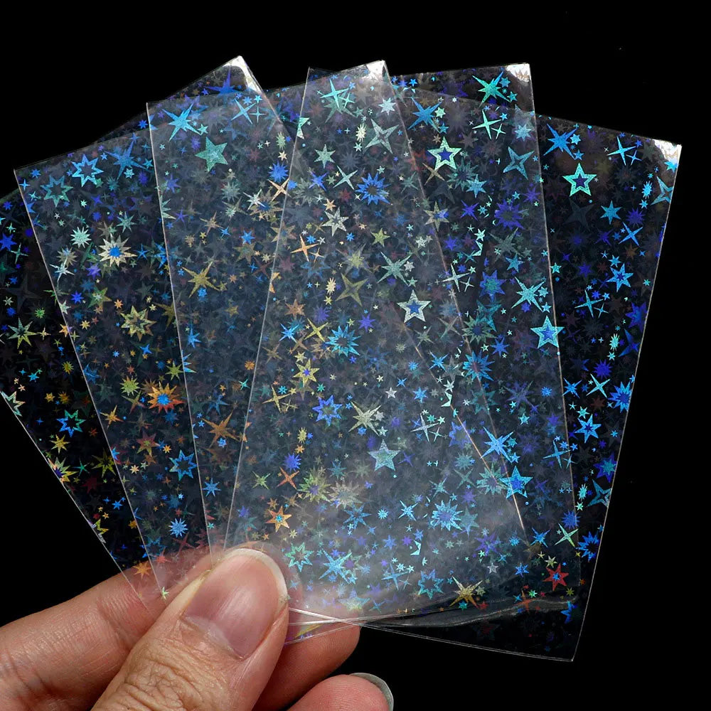 A hand holds several holographic card sleeves with blue and gold star patterns.