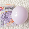 A package of pastel pink latex balloons labeled Feng Che wind balloons resting on a white quilted surface.
