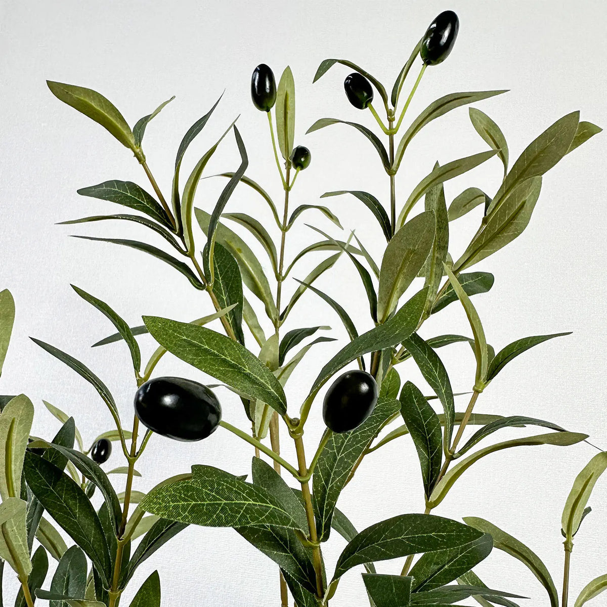 A branch of artificial olive tree leaves and small black olives on a stem.