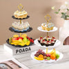 A three-tier plastic dessert stand displaying various cupcakes and fruit on a white surface.