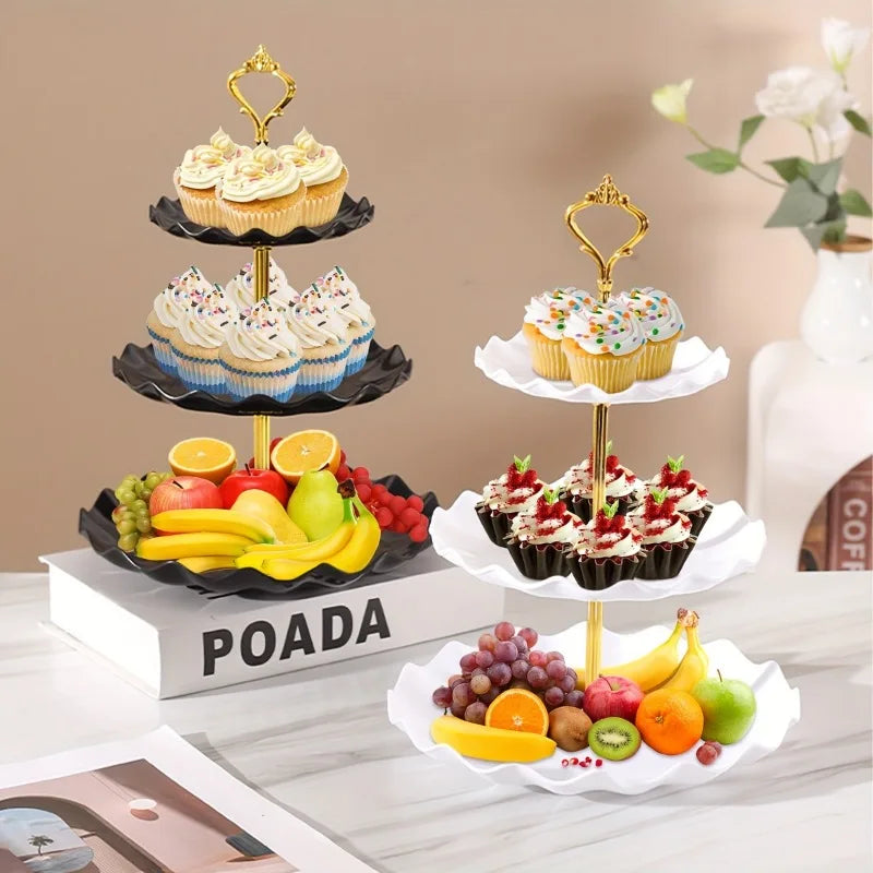 A three-tier plastic dessert stand displaying various cupcakes and fruit on a white surface.