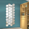 A vertical, irregular hexagon mirror wall decor sticker mounted on a teal wall next to a wooden shelving unit.