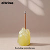 A clear quartz crystal is held by a thin stick, set against a neutral background.
