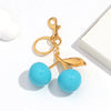 Gold-toned keychain featuring a pink cherry resin pendant with light blue glass beads.