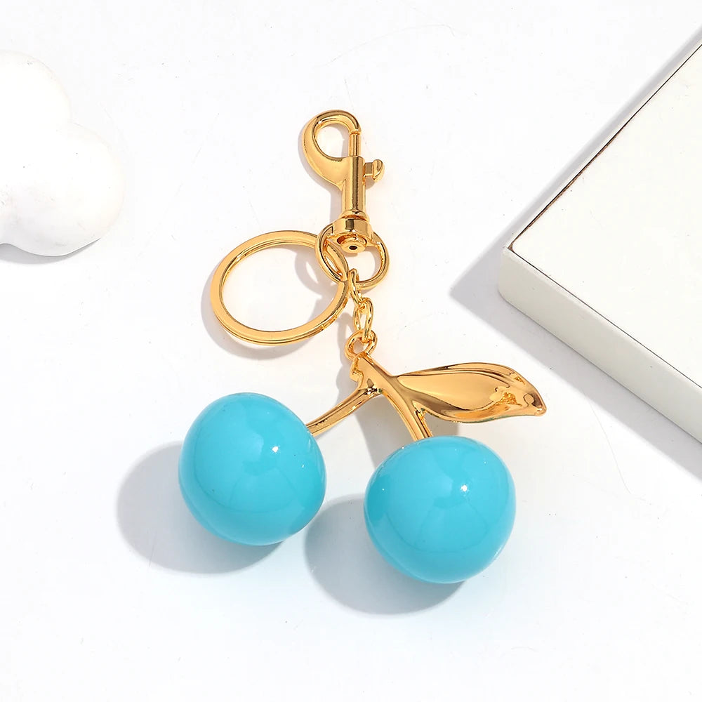 Gold-toned keychain featuring a pink cherry resin pendant with light blue glass beads.