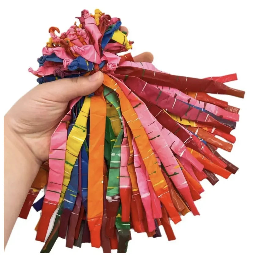 A hand holds a bundle of colorful latex rocket balloons with pink, orange, yellow, and green streamers.