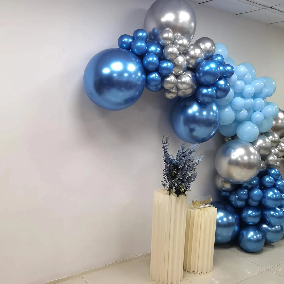 A balloon arch decoration featuring blue and silver balloons on a white wall.