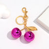 Gold-toned keychain featuring a pink cherry resin pendant on a white background.