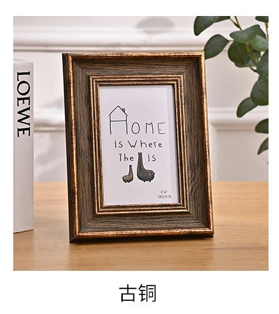 A dark wood photo frame with a gold border displaying the text Home is Where The Is.